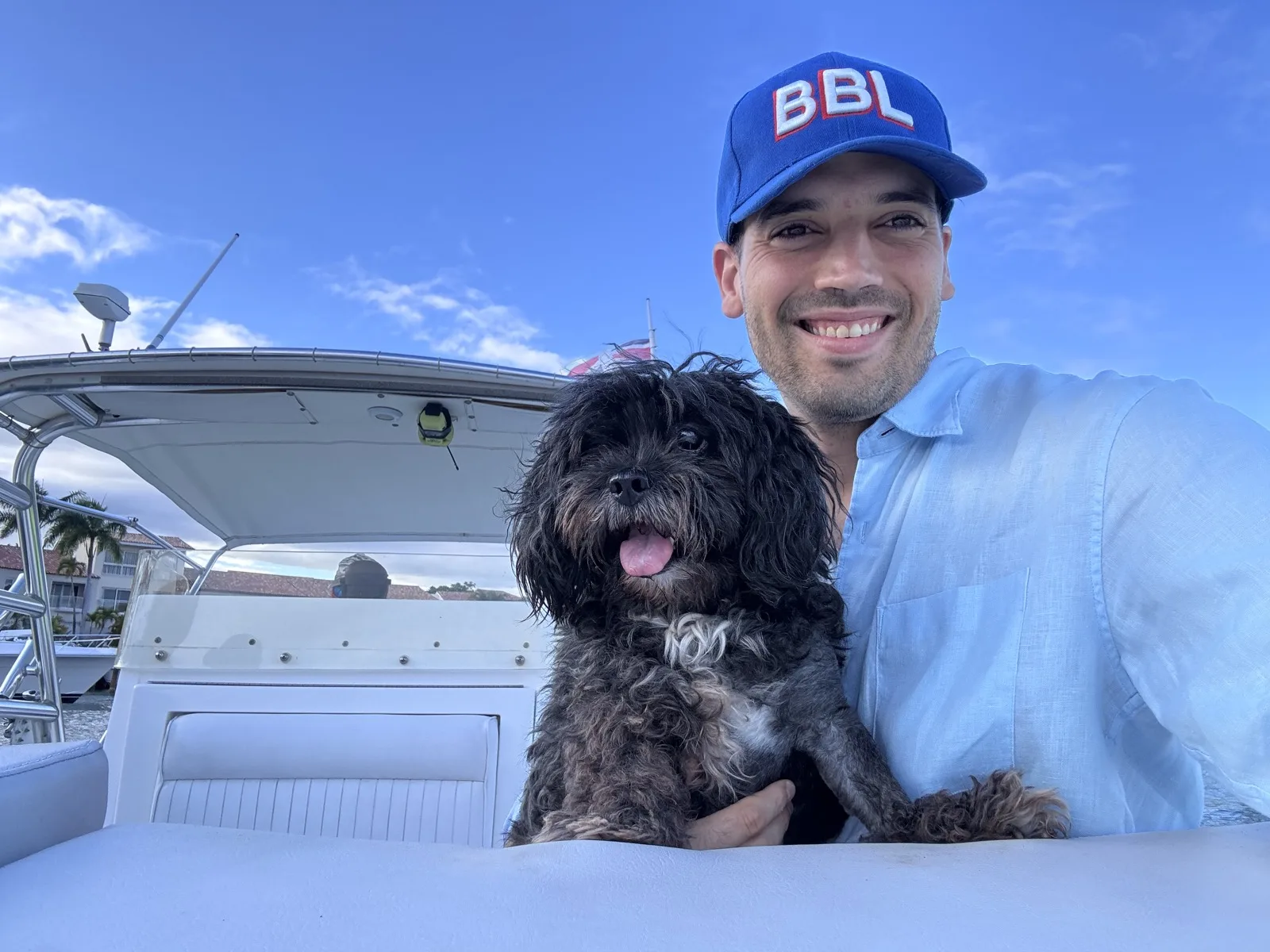 Gustavo sonriendo en un bote junto a su perro, con una gorra de BBL